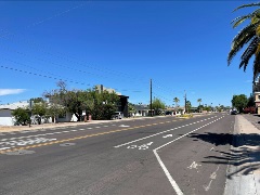 Sunny intersection with palm trees, cars, pedestrian signs, and a mountain in the background.