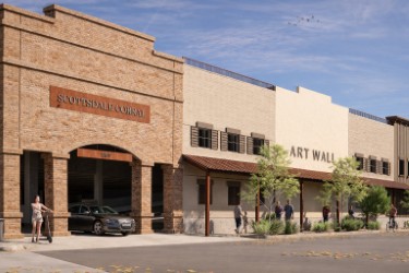Street view of Scottsdale Corners and the Art Wall storefronts, showing brick and stucco facades, small trees, pedestrians, and a parked car along the curb.