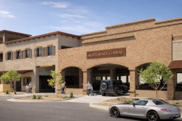 Scottsdale Corral parking structure entrance with a brick facade, parked and passing cars, small trees, and pedestrians along the street.
