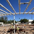 Construction site with workers building a large shade structure, surrounded by construction materials and equipment.