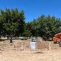 Construction site with an orange crane and workers installing light poles, with trees in the background.