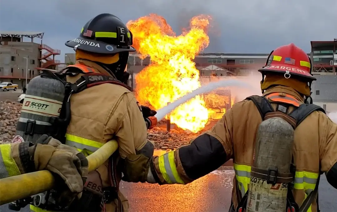 firefighter recruit being trained on using a fire hose while putting out a controlled fire