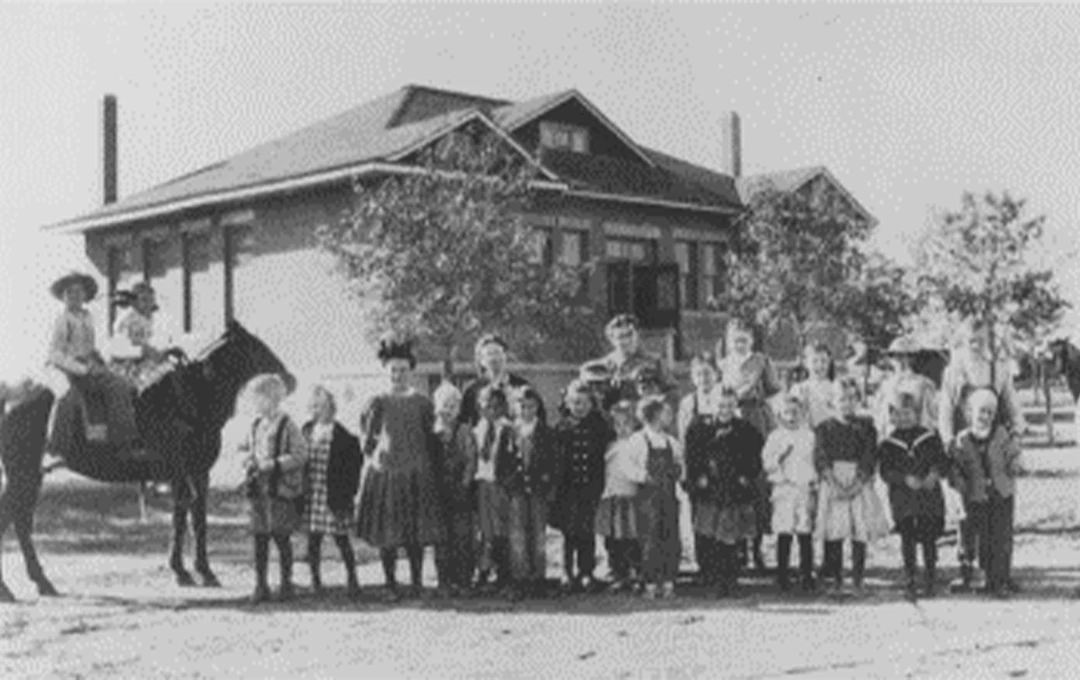 School children and teachers posing for a portrait in front of the old school house.