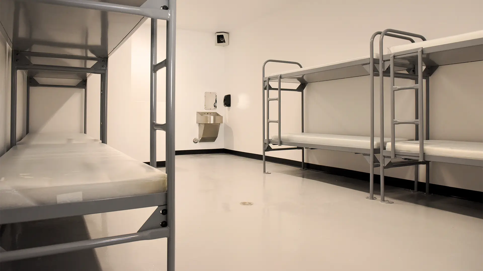 Empty jail cell dormitory with metal bunk beds and a stainless steel sink toilet combo.