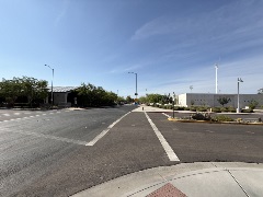 Wide intersection with freshly paved roads, crosswalk markings, landscaped medians, and low modern buildings surrounded by desert plants under a clear sky