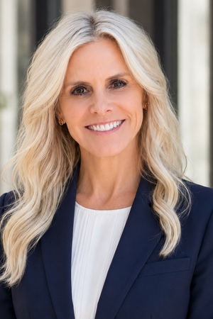 Professional headshot of Judy Doyle smiling, wearing a navy blazer and white top.