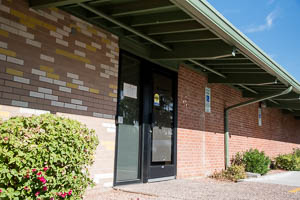 Brick community office building with glass entrance, green awning, and surrounding desert landscaping.