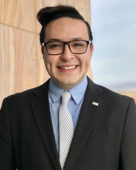 An outdoor portrait of Representative Brian Garcia smiling in front of a building with marbled walls.