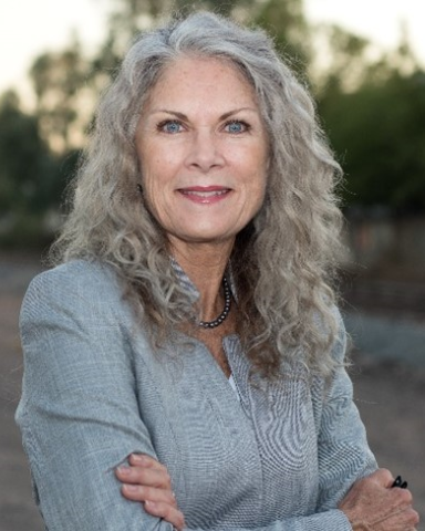 An outdoor portrait of Representative Janeen Connolly smiling in front of some trees.