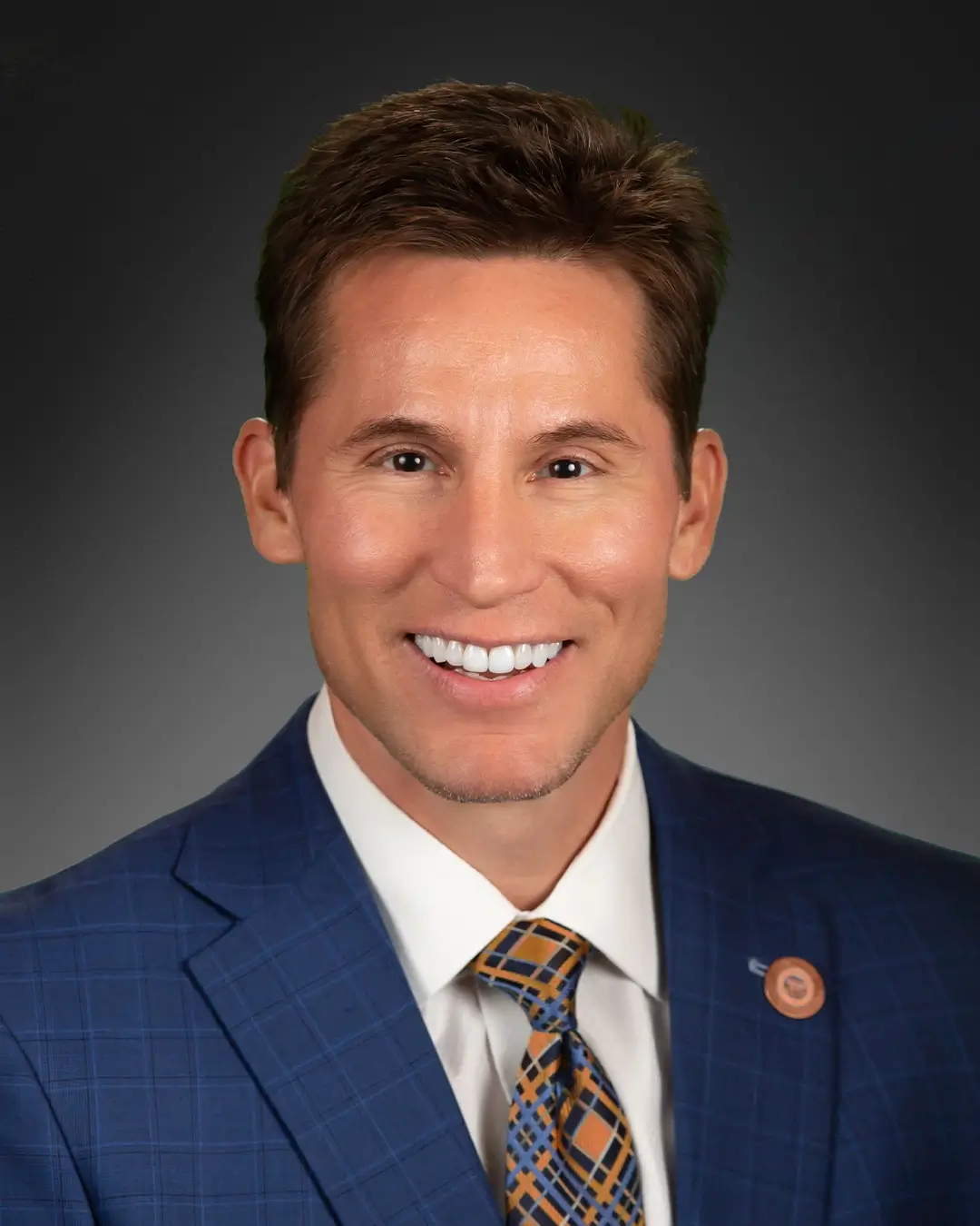 A portrait of Representative Joseph Chaplik smiling in front of a plain background.