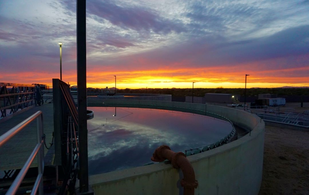 A sunset sky reflected in a large, circular water treatment basin at an industrial plant.