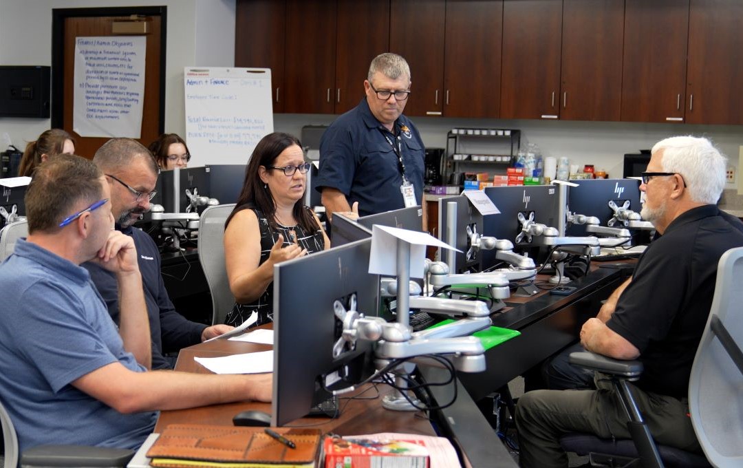 People collaborating at computer workstations during an emergency management training session.