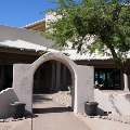 A stucco archway with potted barrel cacti leads to the covered entrance of a southwestern-style building.