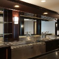 A bar with stainless steel counters, beer taps, glass shelves, wall sconces and a mirrored back wall.