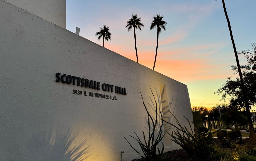 Scottsdale City Hall sign on a white wall with palm trees at sunset.