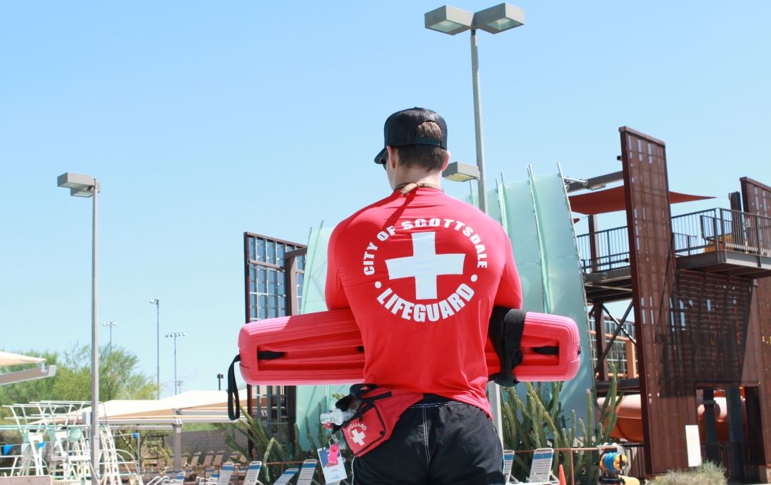 City of Scottsdale lifeguard standing with a rescue tube at an outdoor aquatic center.