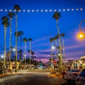 Old Town Scottsdale street at dusk with palm trees wrapped in string lights, parked cars, and shops under a purple and blue sky.