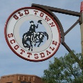 Round Old Town Scottsdale sign with a cowboy riding a bucking horse, mounted on a wooden post.