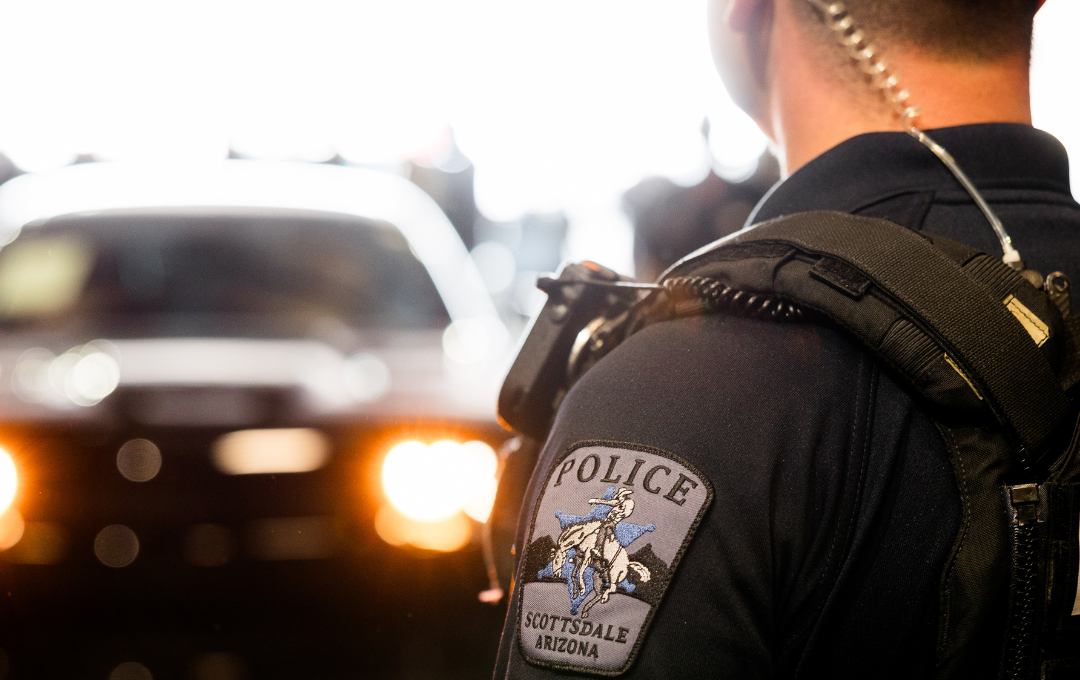 Police uniform close-up showing a Scottsdale police patch with a blurred vehicle in the background