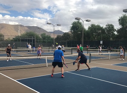 People actively playing pickleball on multiple outdoor courts with mountains and trees in the background.