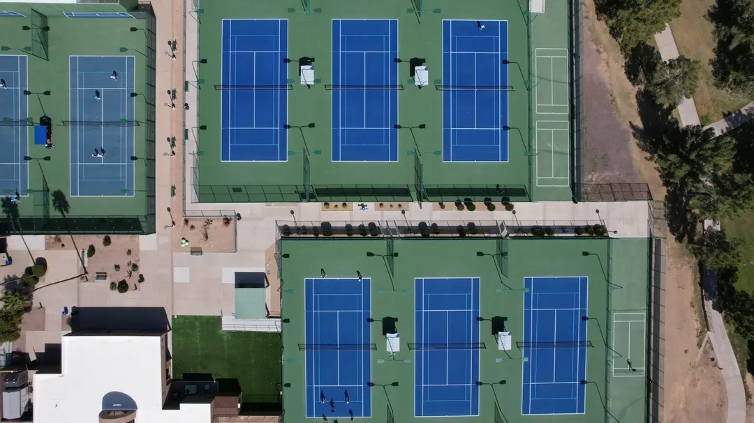 Aerial view of multiple blue-and-green tennis courts arranged in rows at a large sports facility.