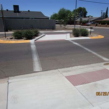 Crosswalk with a pedestrian refuge island, curb ramps, and detectable warning pads on a neighborhood street.
