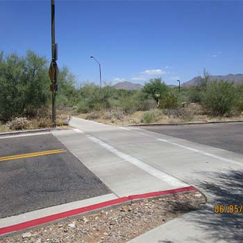 Raised pedestrian crossing on a desert-edge roadway, with curb ramps, sidewalk connection, and low vegetation with mountains in the background.