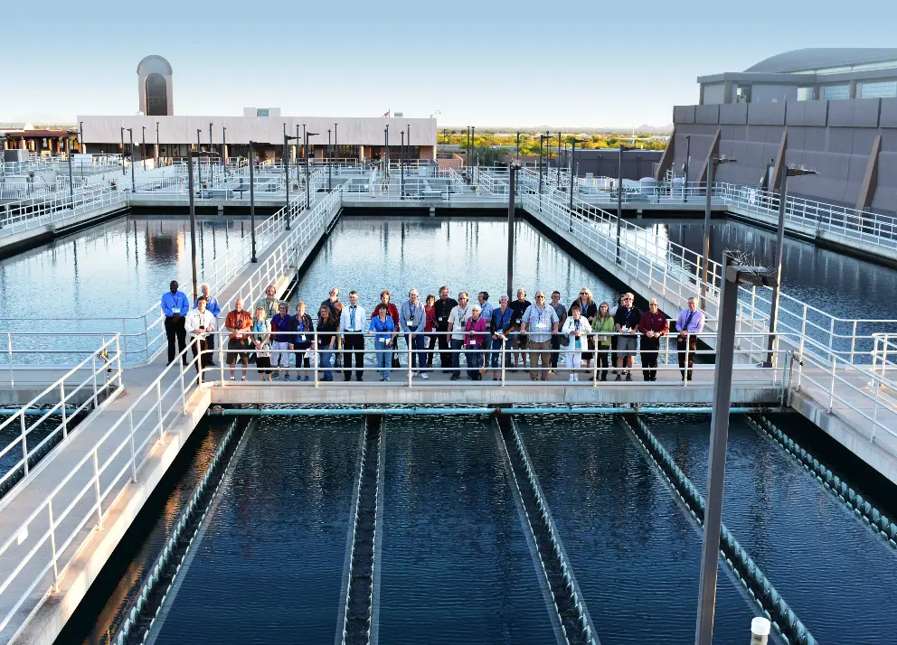 A large group of people pose for a photo on a walkway at a water treatment plant.